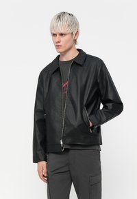 Black leather jacket with a straight cut, zippered front, and side pockets. Features a collared neck and smooth texture.