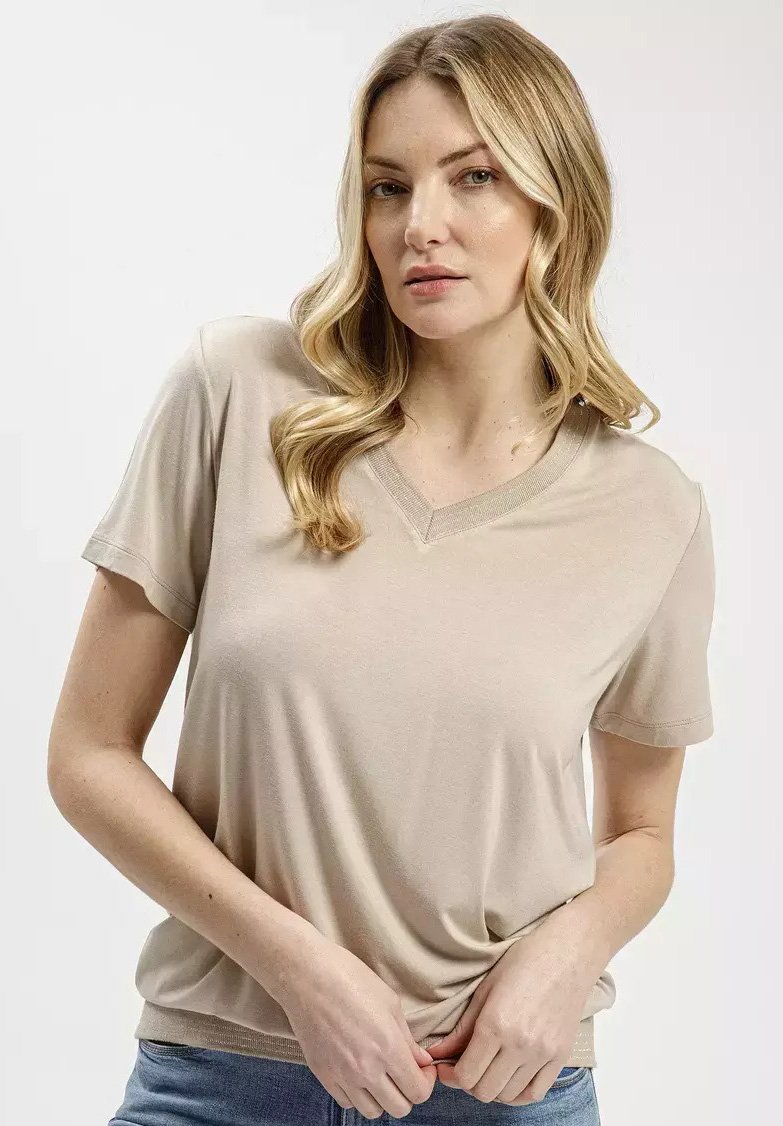 Beżowy t-shirt z krótkim rękawem i dekoltem w serek, wykonany z miękkiego materiału, wyróżniający się subtelną fakturą i lekko dopasowanym krojem, zestawiony z niebieskimi dżinsami.