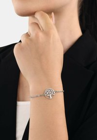 Bracciale d'argento con un pendente circolare decorato con un motivo ad albero, montato su una delicata catena, indossato su un polso.