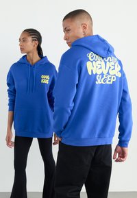 Blue hoodies made of cotton blend; front has "COOL KIDS" in yellow; back features "NEVER SLEEP" in bold yellow text. Kangaroo pocket.