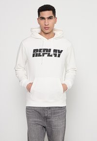 Weißer Hoodie mit einem großen schwarzen "REPLAY"-Logo auf der Vorderseite. Er hat eine Fronttasche und verstellbare Kordeln für die Kapuze.