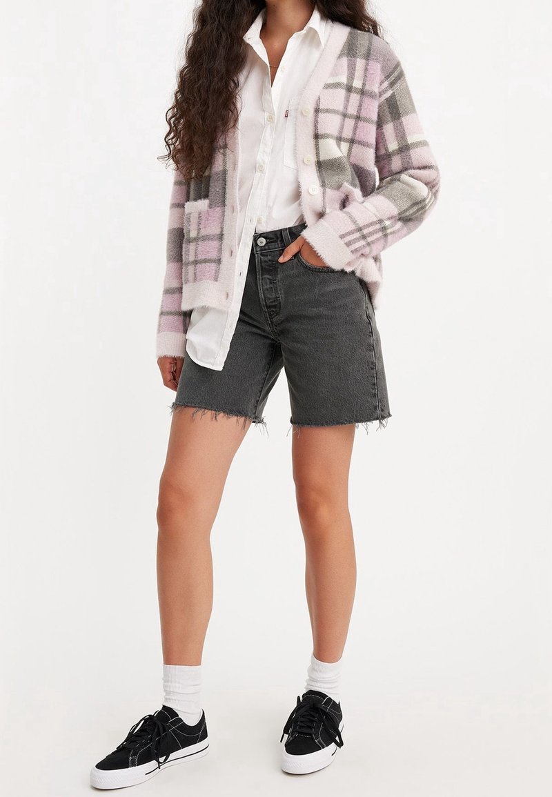 Cardigan de cuadros rosa y gris, camisa blanca, pantalones cortos de mezclilla negros, zapatillas negras con suelas blancas y calcetines blancos hasta la mitad de la pantorrilla. Atuendo casual.