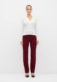 Maglietta bianca a maniche lunghe con scollo a V e dettagli arricciati, abbinata a pantaloni aderenti bordeaux e décolleté nere a punta.