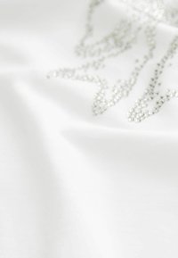 Un tissu blanc avec une texture lisse présente un design d'embellissement argenté scintillant, créant un éclat subtil avec des éléments décoratifs dispersés.