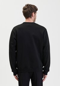Zwarte sweatshirt met lange mouwen, een ronde hals en een relaxte pasvorm. Vloerbare stof met ribbels bij de manchetten en de zoom. Eenvoudig, effen ontwerp.