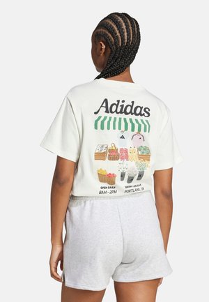 Hell gefärbtes, kurz geschnittenes T-Shirt mit "Adidas"-Logo und Grafik eines Marktes auf der Rückseite; kombiniert mit grauen Shorts. Aus Baumwollmaterial, lässiges Design.