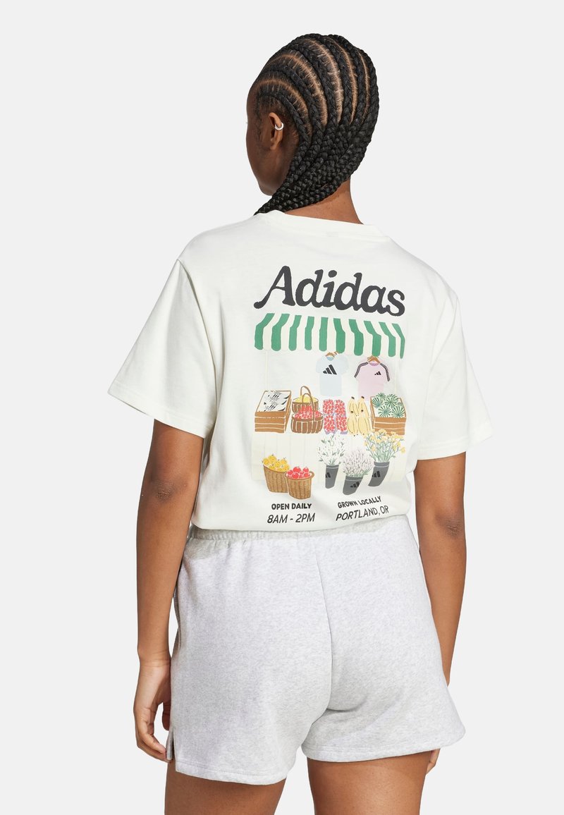 Light-colored cropped t-shirt with "Adidas" logo and graphic of a market on the back; paired with gray shorts. Cotton material, casual design.