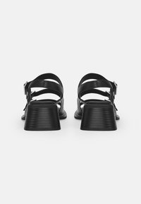 Black leather sandals with wide crisscross straps, adjustable buckles, and a chunky textured heel. Rounded toe and flat sole.
