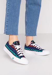 Schwarze und farbenfrohe Sneaker mit Zickzackmuster, weißer Schnürung und Gummisohlen, die eine Gummikappe und einen kleinen blauen Stern-Akzent aufweisen.