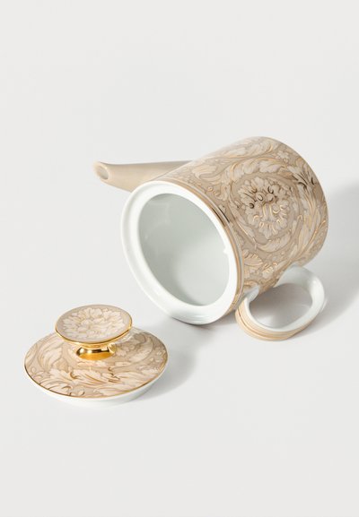 Teapot with beige and gold floral design, shown lying on its side with matching lid placed beside it on a white surface.