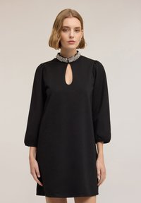 Czarna sukienka z dekoltem w kształcie łezki i ozdobnym ko�łnierzem. Długie bufiaste rękawy i luźne dopasowanie dopełniają projekt. Gładka faktura tkaniny.