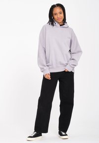 Haut à capuche violet clair à coupe décontractée, avec des poignets côtelés et un cordon de serrage. Associé à un pantalon large noir et des baskets noires.