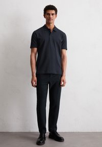 Navy short-sleeve polo shirt with a textured finish, paired with dark slim fit trousers and black leather shoes. Solid color, classic collar design.