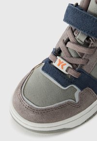 Sivá a námornícka športová obuv z zamšovej kože s suchým zipsom, textilnými šnúrkami, gumovou podrážkou a oranžovým logom značky na hornej strane.
