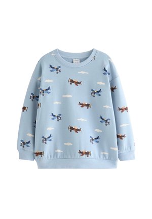 Bambino piccolo che indossa un cappello blu, una felpa con stampa di aerei, pantaloni a quadri blu e bianchi e scarpe da ginnastica marrone chiaro, in piedi su sfondo bianco.