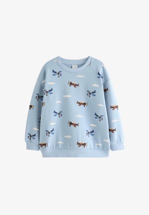 Young child wearing a blue hat, airplane-print sweatshirt, blue and white checkered pants, and light brown sneakers standing on a white background.