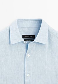 Chemise en lin bleu clair avec un col classique à revers, fermeture à boutons sur le devant et une finition en tissu texturé. Étiquette indique "Massimo Dutti."