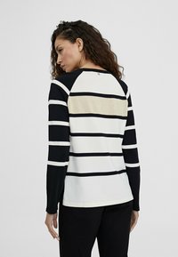 Långärmad topp med marinblå och vita horisontella ränder och en guldaccent på baksidan. Tillverkad av mjukt, elastiskt tyg.