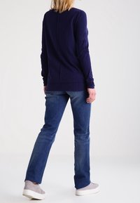 Maglietta a maniche lunghe color navy, in tessuto morbido, con scollatura tonda e dettaglio di cucitura sul retro. Abbinata a jeans azzurri chiari e sneakers grigie.