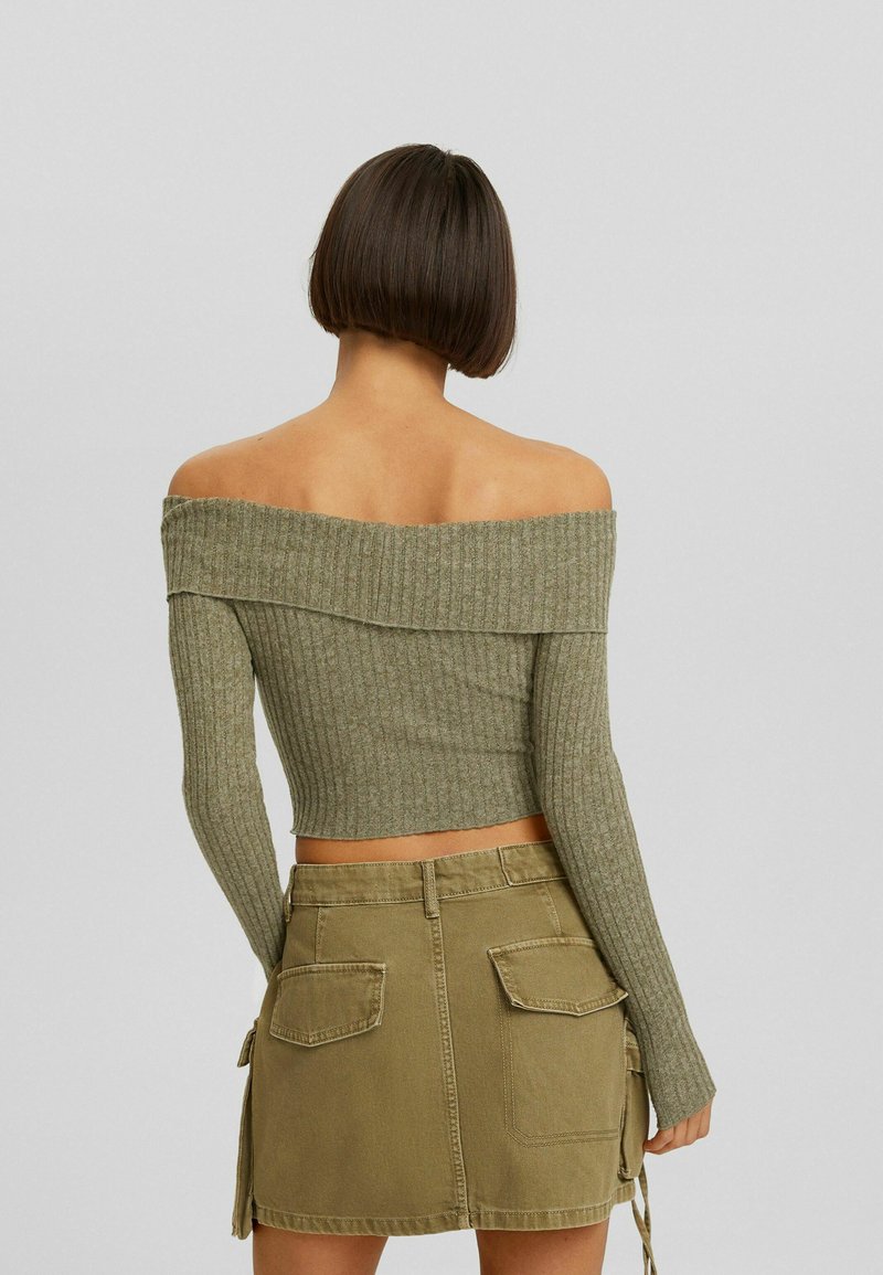 Maglione a coste verde oliva, con scollo off-the-shoulder, maniche lunghe e lunghezza cropped, abbinato a una mini gonna in denim khaki con tasche.