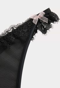 Bralette en dentelle noire avec un tissu doux et texturé. Présente un bord en dentelle festonné et un petit accent en ruban rose sur la sangle.
