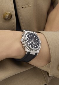 Chronografické hodinky so strieborným puzdrom z nehrdzavejúcej ocele, čiernym ciferníkom a gumeným remienkom, so svetelnými značkami a viacerými subciferníkmi.