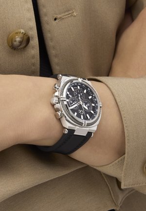 Zegarek chrono z srebrną kopertą ze stali nierdzewnej, czarną tarczą i gumowym paskiem, z luminescencyjnymi znacznikami i wieloma małymi tarczkami.