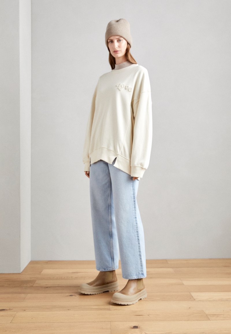 Felpa oversize crema con ricamo "love", jeans dritti azzurro chiaro e scarpe slip-on beige, completati da un berretto in maglia beige.