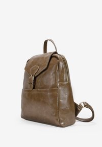 Mochila de cuero marrón con cierre de solapa, bolsillo delantero y correa ajustable. Textura suave con un acabado ligeramente brillante.