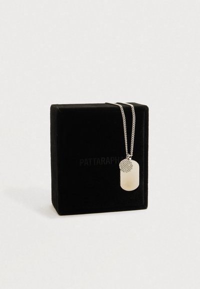 Stříbrný řetízek s dvěma přívěsky, jeden kruhový s texturou a druhý hladký obdélníkový, vystavený na černé semišové krabičce.