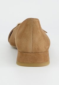 Chaussure en daim beige avec un talon arrondi, une texture lisse et un design minimaliste. Présente un détail de couture subtil à l'arrière.