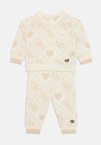 Strick-Zweiteiler in Creme, mit einem Rautenmuster in Beige, das Logos, Herzen und Sterne zeigt; goldene Akzentuierung an den Hosen.