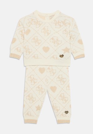 Strikket sæt i creme, med et diamantmønster i beige, der har logoer, hjerter og stjerner; guldaccent på bukserne.