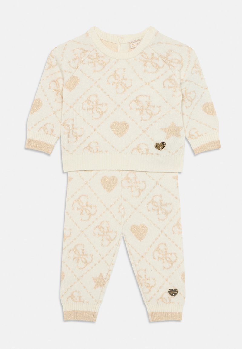 Pleteni dvodelni komplet v krem barvi, s piramidnim vzorcem v bež barvi, ki vključuje logotipe, srca in zvezde; zlat poudarek na hlačah.