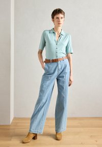 Heledad siniste varvases pluus, millel on nupud ees. Kõrge vöökoht ja heledad teksapüksid, mis on laiad jalgade alt ja millel on pruun nahkvöö. Pruunid kontsaga ankle-boots. 
