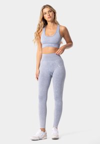 Gaiši zila sporta komplekts, kas sastāv no īsa raga topa un augsta vidukļa legingiem, izgatavots no mīksta, teksturēta auduma ar diskrētām motīvu akcentiem.