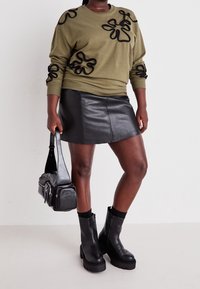 Oliwkowa zielona bluza z czarnymi aplikacjami kwiatowymi, czarna mini spódnica ze skóry, czarne botki na masywnym obcasie oraz czarna torebka na ramię.