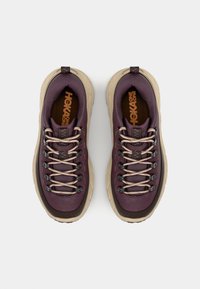 Sneakers HOKA One One z purpurową cholewką, beżową gumową podeszwą i teksturowanym wykończeniem. Posiadają beżowe sznurowadła i czarne oczka.