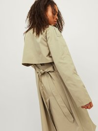 Beige Trenchcoat mit tailliertem Schnitt und ausgestelltem Design. Verfügt über einen Rückenkapuze, lange Ärmel und eine gürtelförmige Bindung. Glatte Stofftextur.