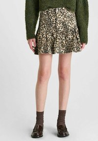 Leopardprint spijkerrok met een uitlopende zoom, voorzien van een aangesloten tailleband en zichtbare knopen aan de voorkant. G gedragen met een groene textuurtrui en donkere sokken.