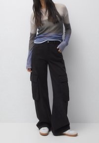 Gebreide trui met verloopkleuren van beige naar blauw, gecombineerd met losse zwarte cargobroek met zijzakken en een knoopsluiting.