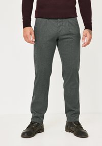 Grau strukturierte Hose mit geradem Bein und dezenten Falten, kombiniert mit schwarzen Schnürstiefeln. Die Kleidung ist figurbetont und modern.