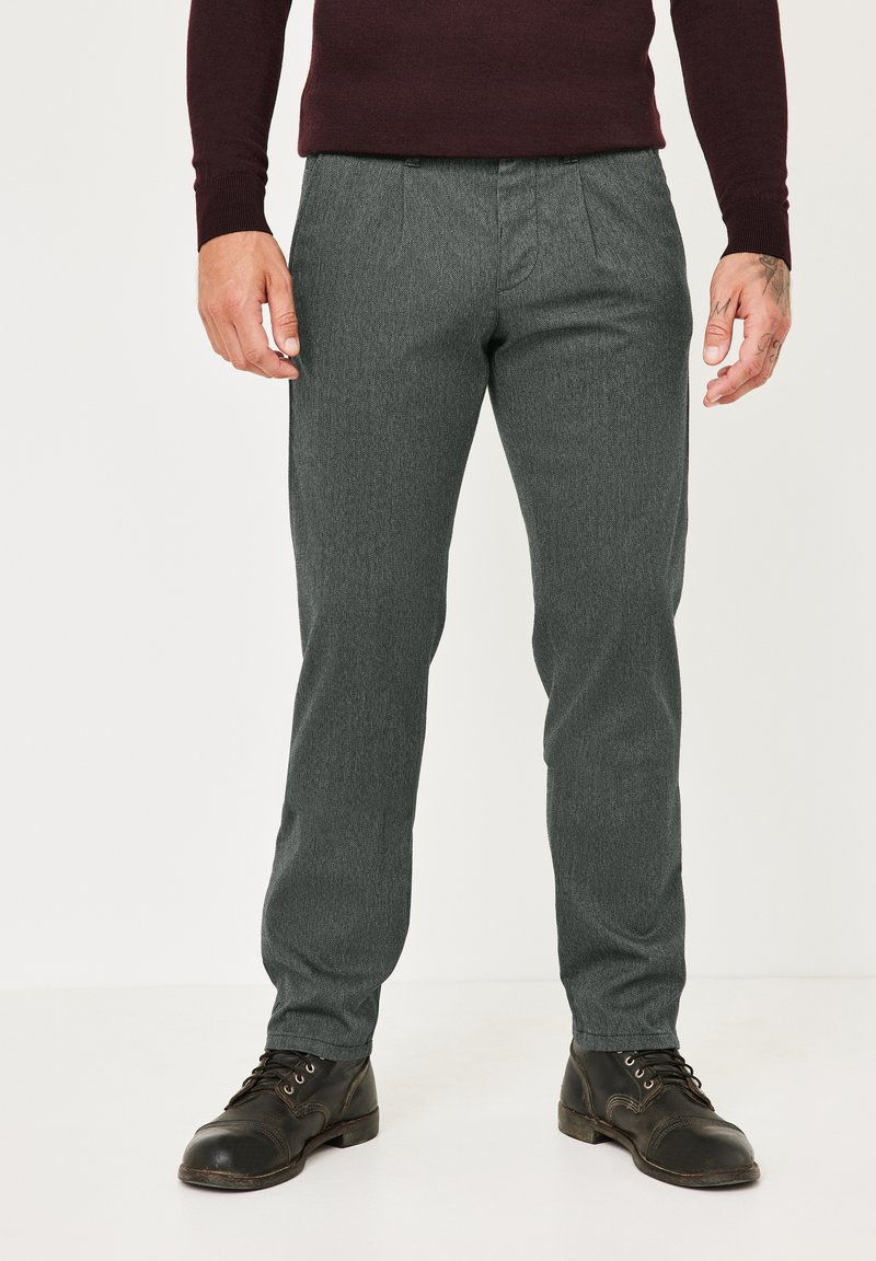 Grau strukturierte Hose mit geradem Bein und dezenten Falten, kombiniert mit schwarzen Schnürstiefeln. Die Kleidung ist figurbetont und modern.