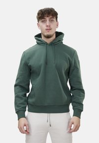 Felpa verde con tasca a marsupio frontale, cappuccio con cordino e polsini a costine. Realizzata in tessuto morbido con una finitura leggermente strutturata.