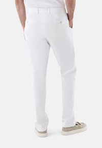 Weiße Hose im Slim-Fit-Schnitt, mit zwei Gesäßtaschen, einem Knopfverschluss und einer glatten Textur, kombiniert mit hellen Schuhen.