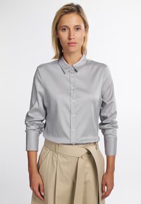 Grå button-up skjorte med klassisk krave, lange ærmer og en glat tekstur. Parret med beige høj talje bukser med et bredt bælte.