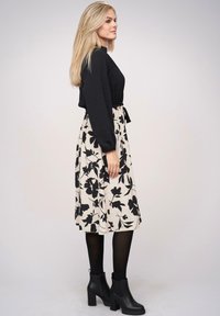 Maglia nera a maniche lunghe abbinata a una gonna midi beige con motivo floreale e stivali neri alla caviglia. Presenta una texture liscia e una vita aderente.