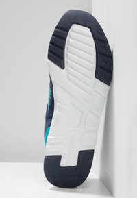 Urheilukenkä, jossa tummansininen yläosa, teal-väriä korostavia yksityiskohtia ja teksturoitu valkoinen kumipohja, jossa on kuvioitu kulutuspinta pitävän otteen takaamiseksi.