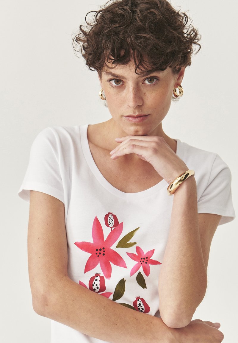 White cotton t-shirt with short sleeves, featuring a floral print in pink and green. Rounded neckline, soft texture, and fitted design.