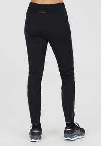Svarta atletiska leggings med en skräddarsydd design, elastiskt midjeband och blixtlåsdetaljer vid anklarna. Slät tyg med subtil textur.
